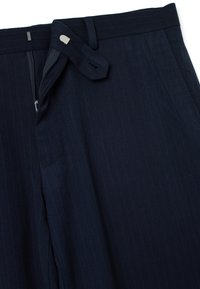 Pantalones de raya diplomática azul marino con cierre de cremallera y botón a presión, cintura plana y presillas para cinturón. Confeccionados en una tela lisa con textura suave.