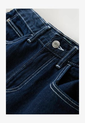 Jeans di denim blu scuro con cuciture bianche, chiusura con bottone in metallo e tasche anteriori, vista ravvicinata della zona della vita.