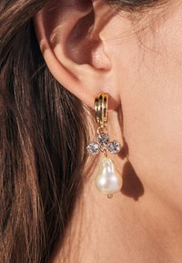 Gold hoop earrings featuring three clear crystals and a teardrop-shaped pearl. The design combines metallic shine with smooth, glossy pearl texture.