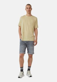 Hellbeige Kurzarm-T-Shirt, grau denim Shorts mit umgeschlagenem Saum, schwarz-weiße gestreifte Socken und neutrale Sportschuhe.