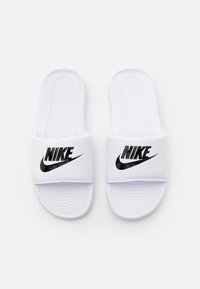 White slide sandals with a textured sole, featuring a wide strap embossed with a black Nike logo. Smooth plastic material and minimalistic design.