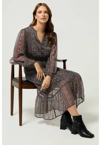 Vestido de manga larga de gasa negra con estampados en rosa y crema, con escote en forma de V y falda de volantes, combinado con botas negras hasta el tobillo.