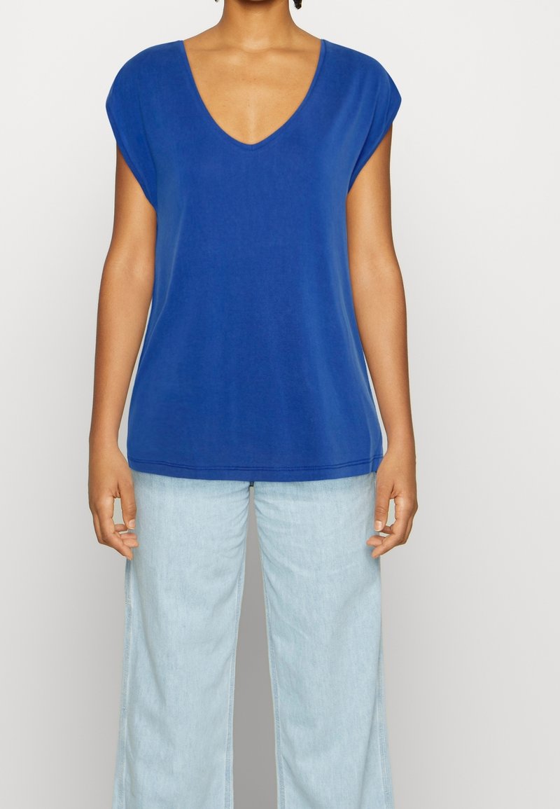 Blue, short-sleeved top with a V-neck, made of smooth fabric. Paired with light blue wide-leg jeans; simple design with no patterns.