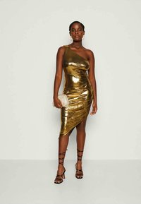 Zlata ena rame oblečena obleka s fitted, drapirano zasnovo in asimetričnim robom. Gladek, sijoč material v kombinaciji s črnimi sandali na vezalke in večernim nahrbtnikom.