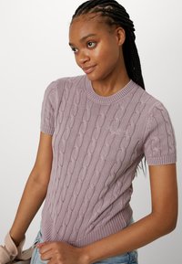 Kortärmad, kabelstickad tröja i ljus lavendel, med ribbat halsband och nederkant, tillverkad av mjukt, texturerat material.