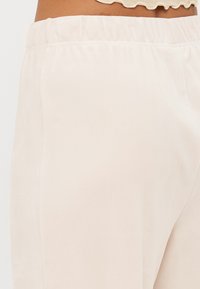 Calças de tecido suave bege claro com cintura elástica; textura lisa; design minimalista sem bolsos visíveis ou detalhes adicionais.