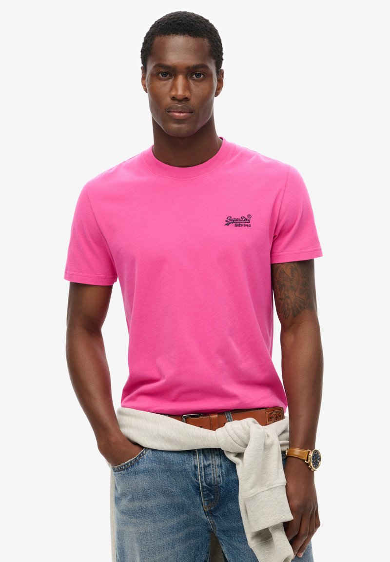 T-shirt in cotone rosa con maniche corte e colletto girocollo, caratterizzata da un piccolo logo nero sul petto. Felpa grigia chiara legata in vita.