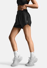 Svarta sportshorts med hög midja, sidorevor och logodetalj. Matchas med vita sportskor och strumpor.