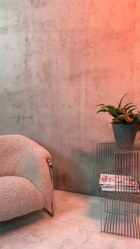 Fauteuil texturé et confortable à côté d'une table d'appoint en fil de fer avec une plante en pot et des magazines empilés contre un mur en béton.