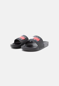 Black slide sandals with a wide strap featuring a red and white logo design. Smooth texture and flat sole for casual wear.