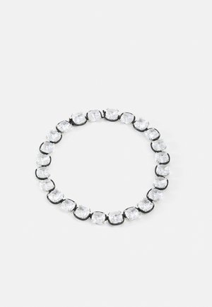 Bracelet rond avec de grandes pierres précieuses carrées claires serties dans des maillons en métal noir sur un fond gris clair.