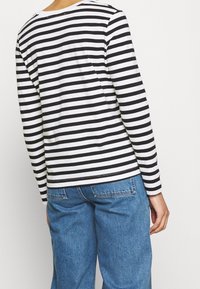 Schwarz-weißer gestreifter Langarmshirt mit einer lockeren Passform, kombiniert mit hellblauen weit geschnittenen Jeans. Das Shirt hat einen runden Halsausschnitt.