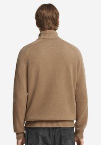 Brun stickad tröja med hög krage, ribbade muddar och nederkant. Mjuk textur och åtsittande design med raglanärmar.