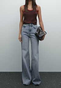 Bruine tanktop met rode bies, lichtblauwe high-waisted flare jeans, zwarte handtas met zilveren accenten, staand op een gestructureerd oppervlak.
