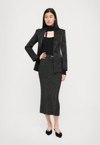 Black patterned blazer over a black ribbed top, paired with a dark grey shimmering midi skirt. Black pointed-toe heels complete the outfit.