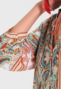 Long-sleeve blouse featuring a colorful paisley pattern in shades of orange, teal, and brown, with buttons at the cuff and a lightweight fabric.