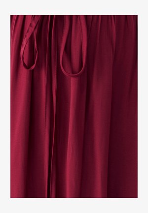 Burgundská tkanina s jemnou textúrou, s naťahovacím pásom a zaviazanou šnúrkou. Viditeľné sú švy pozdĺž celej dĺžky.