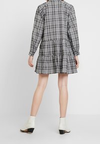 Svart- och vitrutigt klänning med långärmar, en skiktad kjol och knappar bak; matcher med vita anklarstövlar med svart klack.