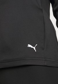 Schwarzes Sportoberteil mit glatter Textur. Verfügt über ein weißes Puma-Logo an der unteren Seite und ein einfaches, figurbetontes Design.