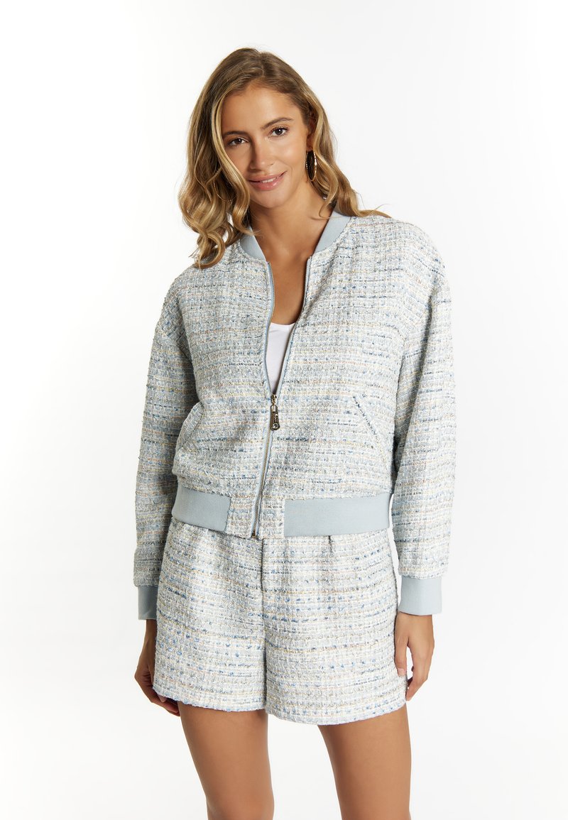  Lichtblauwe tweed bomberjack met gestructureerd ontwerp, ritsluiting en geribbelde mouwen. Gecombineerd met bijpassende textuurshorts.