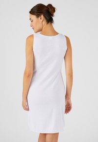 Robe blanche sans manches en tissu doux, dotée d'un col rond, d'une fente au dos et d'une coupe décontractée avec une texture lisse.