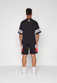 Black short-sleeve shirt features white stripes and a logo at the back, paired with black shorts that have red and white accents.