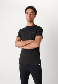 Tricou negru cu mânecă scurtă, din bumbac, având un mic „II” brodat în portocalie pe partea stângă a pieptului, cu gât cu croială rotundă și textură netedă.