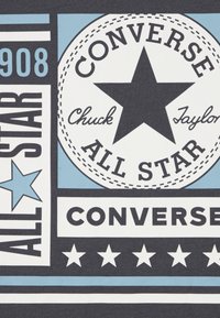 Grafikai nyomat fekete csillaggal, a "CONVERSE" és a "Chuck Taylor" feliratok fekete-fehér színben, világoskék részletekkel sötét háttéren.