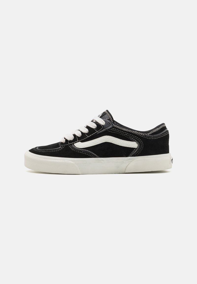 Black suede sneaker with white stitching and side logo, featuring a flat rubber sole and laced design. Accents include a white stripe.