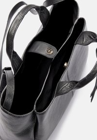 Černá texturovaná kožená kabelka s dvěma uchy a zapínáním na patentku, ukázaná otevřená, odhalující vnitřní oddělení.