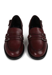 Sapatos de couro bordô com fechos de fivela dupla, biqueira redonda e solas em borracha preta contrastante com detalhes de costura.