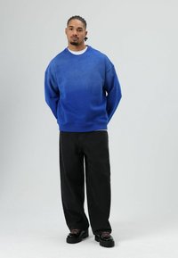 Sweat-shirt bleu à motif dégradé et petits clous noirs, accompagné d'un pantalon noir à jambes larges et de chaussures noires avec des lacets roses.