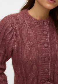 Knitted sweater in soft, textured pink wool with cable patterns and round buttons down the front. Features a crew neckline and gathered sleeves.
