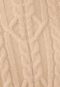 Beige kabelgebreide stof met verweven gedraaide patronen en een zachte, gestructureerde uitstraling, met lichte variaties in dikte.