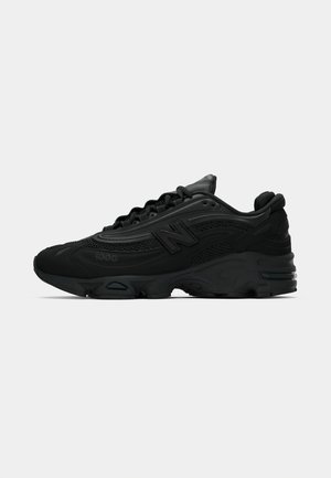 Black athletic sneakers with a textured mesh overlay, rubber sole, and prominent cushioning. Features a logo on the side and lace-up design.