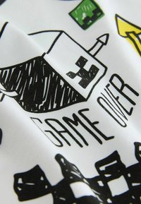 Tissu blanc plié avec des éléments de jeu cartoon noirs et verts, y compris un bateau avec un visage carré et les mots "GAME OVER".