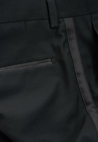 Pantalon noir avec une texture lisse, comportant une poche zippée sur le côté et une bande en satin sur le côté, mise en valeur contre le tissu mat.