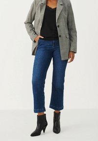 Jasnoszary marynarka w kratę noszona na czarnym topie, w połączeniu z ciemnoniebieskimi, krótko ciętymi dżinsami i czarnymi, spiczastymi botkami za kostkę. Gładkie tekstury i dopasowany krój.