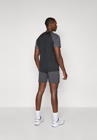 Ensemble de sport masculin comprenant un t-shirt noir à manches courtes avec des accents gris aux épaules et un short gris assorti, conçu pour le confort et la mobilité.