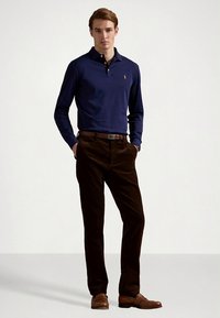 Tengerészkék hosszú ujjú galléros póló barna kordbársony nadrággal és barna bőr cipővel párosítva. A mellkason kis logó található.