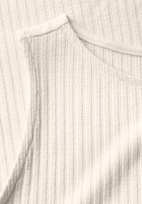 Top sin mangas blanco con un patrón texturizado y acanalado, y escote redondeado. Fabricación suave con un brillo sutil.
