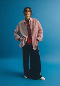 Czerwona i biała w pasy przesadna koszula, czerwona koszulka z grafiką pod spodem, czarne szerokie spodnie z bocznymi paskami i białe trampki.