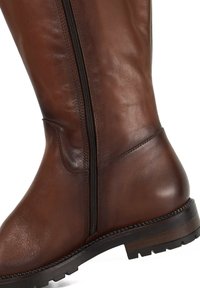 Brown leather knee-high boot featuring a side zipper and a textured surface, with a sturdy black rubber sole and detailed stitching.