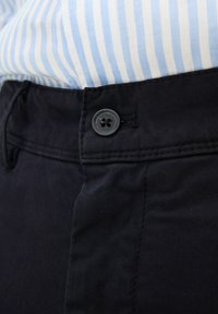 Pantaloni blu navy con una texture liscia, dotati di un bottone di plastica a quattro fori e una vita piatta con dettagli di cucitura visibili.