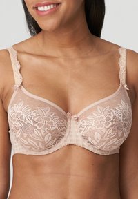 Reggiseno beige in pizzo con ricamo floreale, bordi scallop sulle spalline e piccoli fiocchi al centro e nei punti di transizione delle spalline. Pattern a quadretti testurizzato sulle coppe.