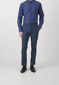 Tmavě modrá košile na knoflíky a odpovídající kalhoty z hladké látky. Černé společenské boty doplňují outfit. Elegantní střih a čistý design.