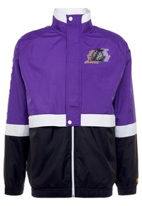 Lila och svart vindjacka med hög krage, vita randiga detaljer och en grafisk design på bröstet. Dragkedjestängning med elastiska manschetter.