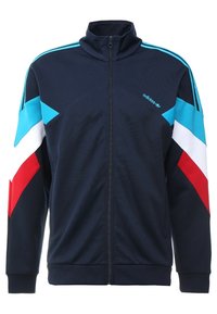 Mörkblå zip-up sportjacka med ljusblå, vita och röda diagonala ränder på ärmarna. Har hög krage och Adidas-logotyp på bröstet.
