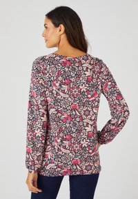 Maglietta a maniche lunghe caratterizzata da un motivo floreale scuro con fiori rosa, rossi e blu. Realizzata in tessuto morbido, con dettagli arricciati sulle spalle.