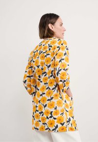 Giacca floreale con un vivace motivo a fiori gialli e bianchi, maniche a tre quarti e tasche laterali. Realizzata in tessuto leggero.